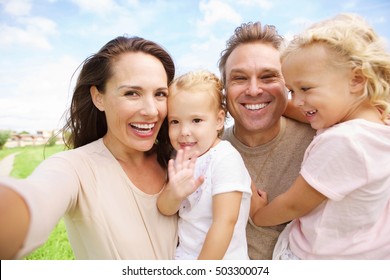 Portrait Of Happy Family With Two Daughters Taking Selfie Outdoors