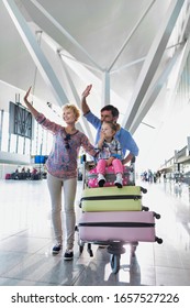 Portrait Of Happy Family Waving In Arrival Area At Airport