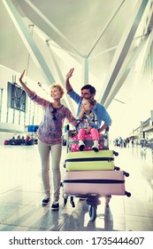 Portrait Of Happy Family Waving In Arrival Area At Airport