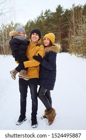 Portrait Of Happy Family In Winter Day Looking At Camera. Mom And Dad Are Cuddling Their Little Son In Winter Park. Family Lovely Moments.