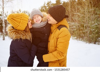 Portrait Of Happy Family In Winter Day. Mom And Dad Are Cuddling And Kissing Their Little Son In Winter Park. Family Lovely Moments, Copy Space