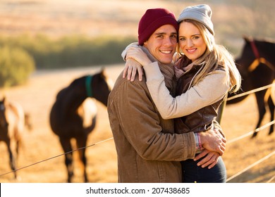 Portrait Of Happy Farm Couple Hugging In Horse Ranch