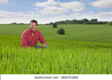 A Portrait of a happy farmer kneeling down in a wheat field with a beautiful landscape in the background