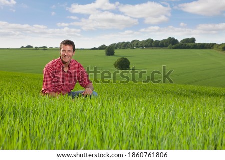 A Portrait of a happy farmer kneeling down in a wheat field with a beautiful landscape in the background