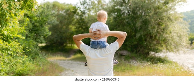 Portrait of happy father giving son piggyback ride on his shoulders. Cute boy with dad playing outdoor.