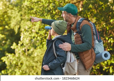 Portrait of happy father and son hiking together and pointing away while walking in forest with backpack, copy space - Powered by Shutterstock