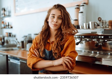 Portrait of a happy female barista standing behind the counter in a coffee shop. A woman cafe owner in an apron looks at the camera and smiles. Business concept. - Powered by Shutterstock