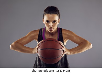 Portrait of happy female basketball player passing the ball. Beautiful young woman in sportswear holding basketball looking at camera against grey background - Powered by Shutterstock