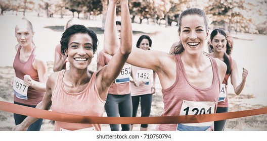 Portrait of happy female breast cancer participants crossing finish line at marathon race in park