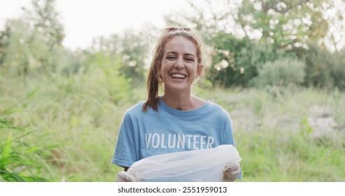 Portrait of a happy female Caucasian volunteer cleaning up a river in the countryside, holding a rubbish bag, smiling and looking at camera. Ecology and social responsibility in a rural environment. - Powered by Shutterstock