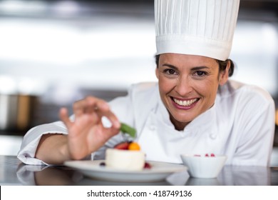Portrait of happy female chef garnishing on food in commercial kitchen