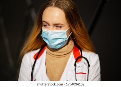 Portrait Of Happy Female Doctor Or Nurse In Surgical Mask And White Medical Gown Looking At You With Wind Picking Up Hair