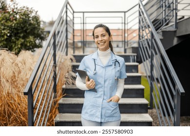 Portrait of happy female doctor with tablet in hands standing on stairs and smiling at camera. - Powered by Shutterstock