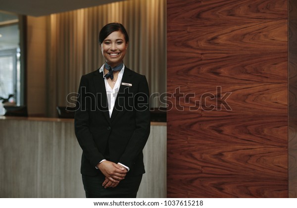 Portrait of happy\
female hotel receptionist standing at workplace. Smiling woman\
receptionist working in\
hotel.