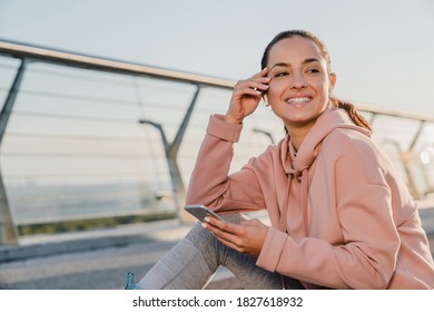 Portrait of a happy female jogger holding her smart phone in pink hoody. - Powered by Shutterstock