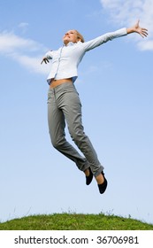 Portrait of happy female jumping over green grass against blue sky