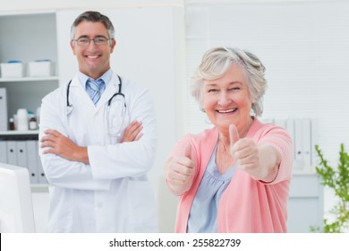 Portrait Of Happy Female Patient Showing Thumbs Up Sign While Standing With Doctor In Clinic