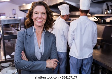 Portrait of happy female restaurant manager standing with arms crossed in commercial kitchen - Powered by Shutterstock