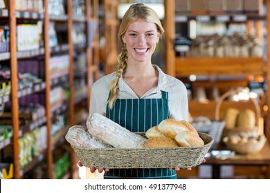 Portrait of happy female staff holding basket of bread at bread counter in supermarket - Powered by Shutterstock