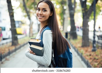 Portrait of a happy female student holding books and looking at camera outdoors