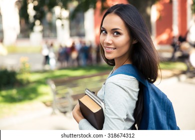 Portrait Of A Happy Female Student Looking Back At Camera Outdoors