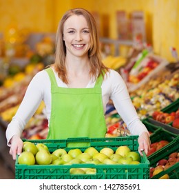 Portrait Of Happy Female Worker Carrying Apple's Crate In Grocery Store