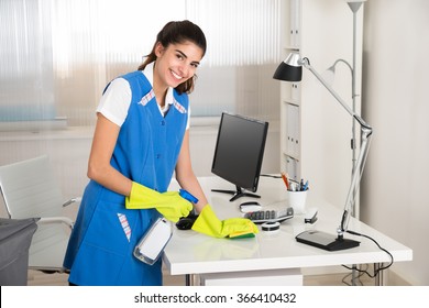 Portrait of happy female worker cleaning computer desk with spray and sponge at office