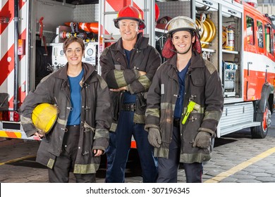 Portrait Of Happy Firefighters Standing Together Against Truck At Fire Station