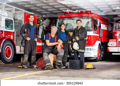 Portrait of happy firefighter's team with equipment against trucks at fire station