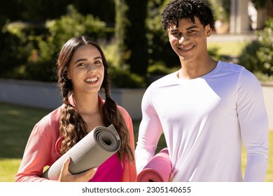 Portrait of happy fit diverse couple standing in sunny garden holding yoga mats. Summer, healthy lifestyle, relaxation and vacations. - Powered by Shutterstock