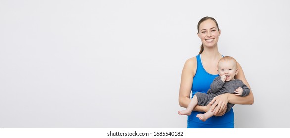 Portrait of happy fit mother and her cute baby looking into the camera, stading on a plain background 