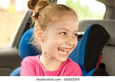 Portrait Of Happy Five Years Old Blond Caucasian Child Girl Laughing While Traveling In A Car Seat