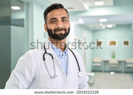 Portrait of happy friendly male Indian latin doctor medical worker wearing white coat with stethoscope around neck standing in modern private clinic looking at camera. Medical healthcare concept.