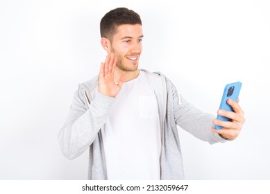 Portrait Of Happy Friendly Young Caucasian Man Wearing Casual Clothes Over White Background Taking Selfie And Waving Hand, Communicating On Video Call, Online Chatting.