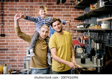 Portrait Of Happy Gay Family Of Two Fathers And Little Boy Standing In Kitchen And Cooking Breakfast