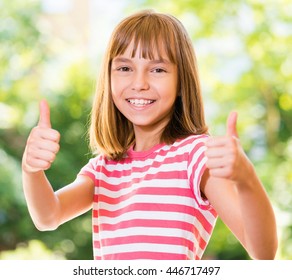 Portrait of happy girl 10-11 year old showing thumbs up gesture. Beautiful schoolgirl posing outdoors.