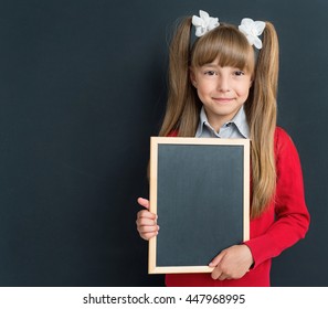 Portrait Of Happy Girl 10-11 Year Old With Small Blackboard In Front Of A Big Chalkboard. Back To School Concept.