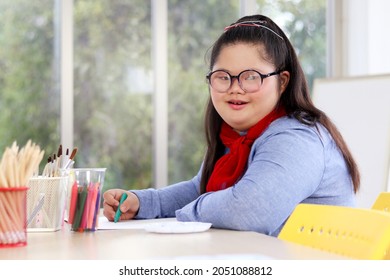 Portrait of happy girl having fun during study at school, child with down syndrome concentrate painting on paper in art classroom, kid with physical disability and intellectual education concept.