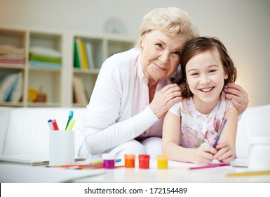 Portrait of happy girl and her grandmother looking at camera at home