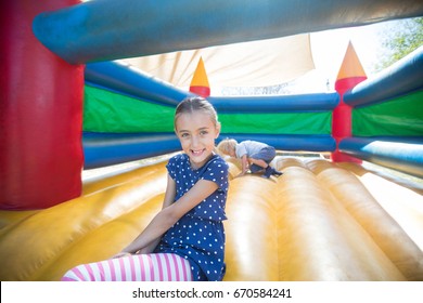 Portrait of happy girl sitting on bouncy castle while brother playing in background - Powered by Shutterstock