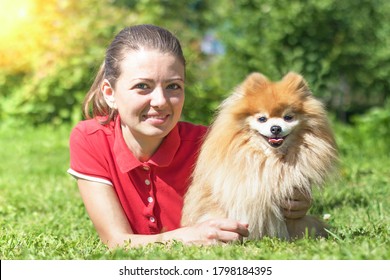 Portrait Of Happy Girl With Spitz Lying On Grass, Looking At Camera. Senior, Adult Dog With Owner. Pet Adoption. Young Woman Walking, Playing In Nature With Pomeranian.