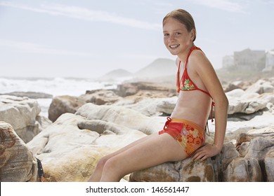 Portrait of happy girl in swimwear sitting on rock at beach