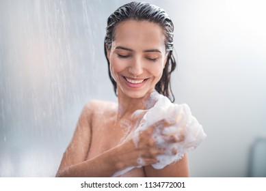 Portrait of happy girl taking shower with gel. She washing with puff - Shutterstock ID 1134772001