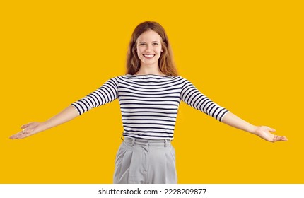 Portrait of a happy, glad, cheerful, positive, friendly woman with a kind, sincere, toothy smile standing on a yellow studio background, spreading her arms wide open to hug you and give a warm welcome - Shutterstock ID 2228209877