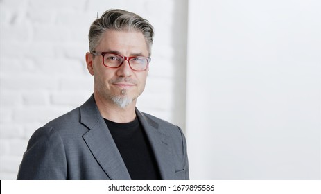 Portrait Of Happy Good Looking Older Businessman In Glasses Wearing Jacket, Smiling In Front Of White Background With Copy Space.  .