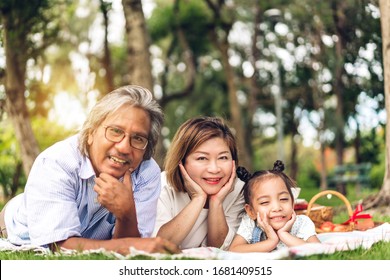 Portrait of happy grandfather with grandmother and little cute girl enjoy relax looking at camara in summer park.Young girl with their laughing grandparents smiling together.Family and togetherness