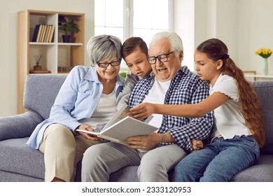 Portrait of a happy grandparents reading a book to their grandchildren or looking through a family photo album sitting on sofa at home. Kids enjoying leisure time with grandma and grandpa on weekend - Powered by Shutterstock