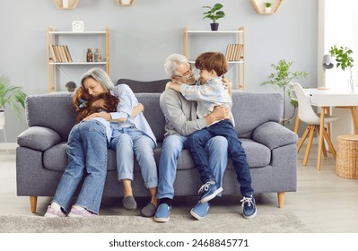 Portrait of a happy grandparents sitting on sofa with their grandchildren boy and girl in the living room at home hugging and smiling. Kids enjoying leisure time with grandma and grandpa. - Powered by Shutterstock