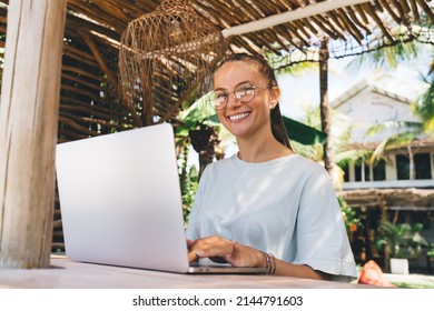 Portrait of happy graphic designer on classic eyeglasses using netbook computer during remote working outdoors, cheerful female copywriter with laptop enjoying digital nomad and freelance lifestyle