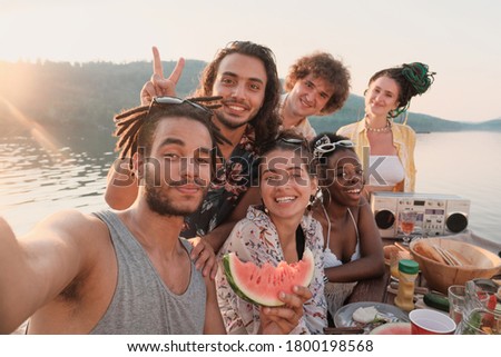 Portrait of happy group of friends smiling and posing at camera they making selfie portrait during picnic outdoors